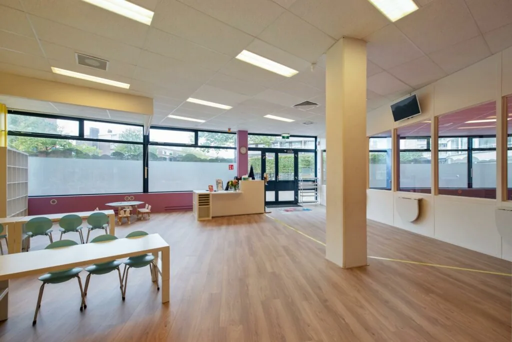 Moderne en lichte wachtruimte of binnenruimte in een kinderopvang aan de Koningin Julianalaan, met speelhoek, kinderstoelen en balie.